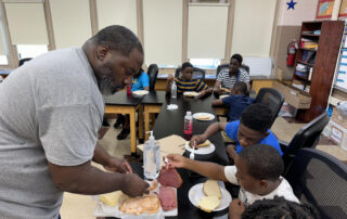 Chef Dex guiding students in food preparation – Chef Dex stands beside a group of middle school students, showing them how to chop vegetables for a healthy recipe, with smiling faces and colorful ingredients on the table.